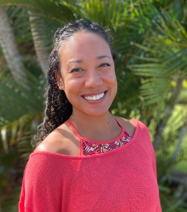 Smiling woman in a pink top standing outdoors with palm leaves in the background