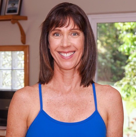 Smiling woman with shoulder-length brown hair wearing a blue tank top indoors